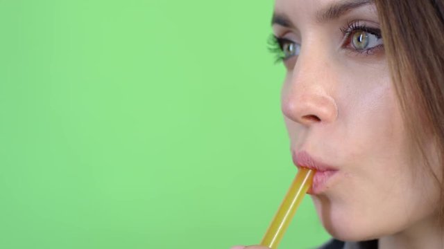 Extreme close up tracking shot of young woman with green eyes drinking freshly squeezed juice using drinking straw