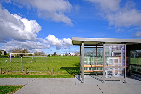 An ordinary bus stop next to a soccer field on a sunny day in Auckland