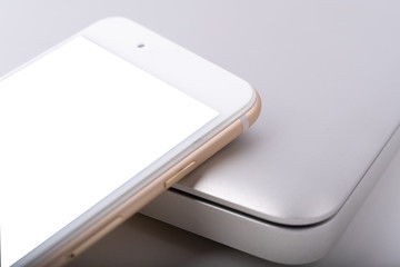 Blank smartphone with white blank screen is put over a laptop.