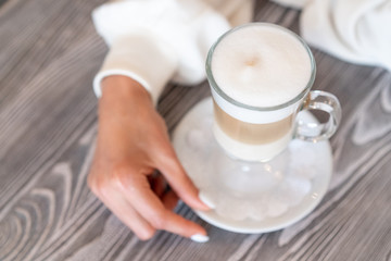 glass latte coffee is standing on wooden table held by girl.