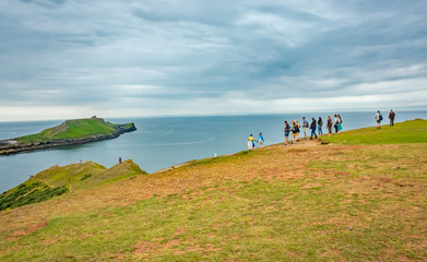 A group of tourists on the cliff tops of the Welsh Coastal path looking out towards Worm’s Head