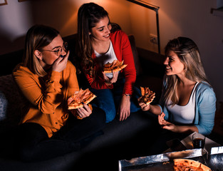 Three female friends chatting and enjoying eating pizza at home.