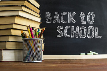 Textbooks and school supplies on a table, against a chalkboard background with chalk. Concept of school with copyspase.