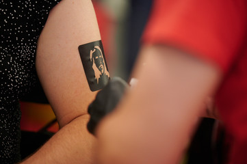 Temporäres Tattoo in Form eines Jesus Kopfes wird per Airbrush auf den Arm gesprüht