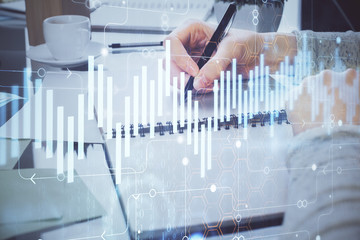 Hand taking notes in notepad. Forex chart holograms in front. Concept of research. Double exposure