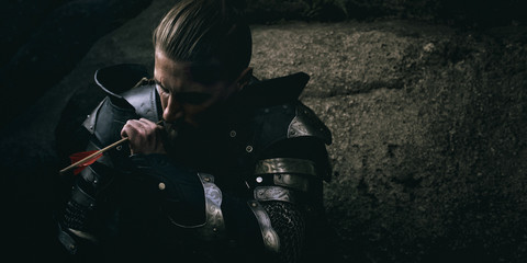 Mystery scarface knight in armor with sword and crossbow in the forest