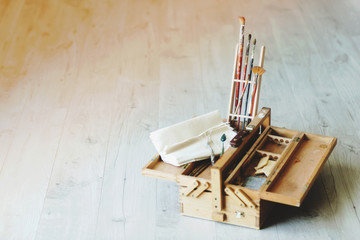 Wooden folding suitcase artist with brushes, paint and canvas. Background of a wooden floor