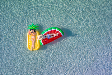 top aerial view of two young women enjoy swimming on floating inflatable tube in sea with cleared water, happy in summertime and vacation or long weekend swimming at sea