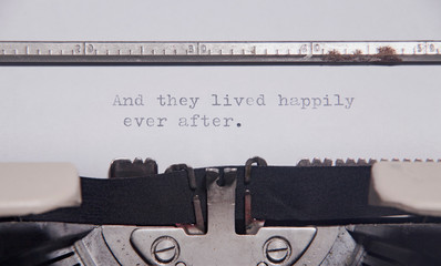 The ending phrase And they lived happily ever after, printed on a paper page inside an old vintage typewriter. Macro close-up shot.