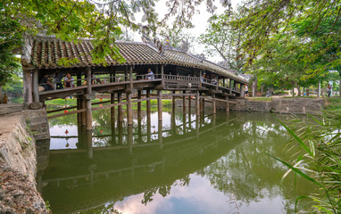 Old wooden bridge crosses the river branch decorated with an upper tile roof dating from the 19th century near Hue city, Vietnam.