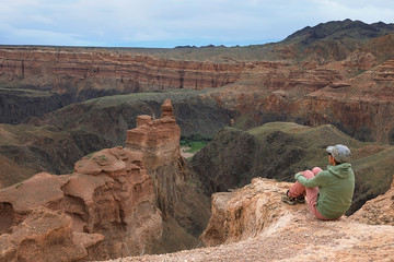 Fototapeta na wymiar Tourist girl sitting on the edge of the canyon Charyn