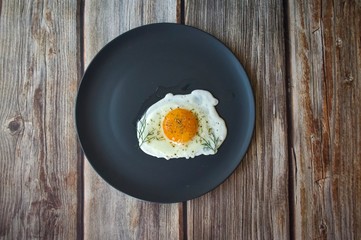 Fried eggs on a black round plate with greens on a brown wooden background