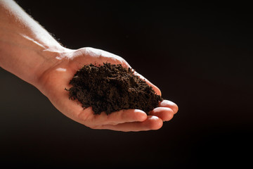 Soil in male hands on dark background ..