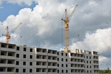 Fototapeta premium Yellow cranes and the construction of prefabricated houses on a background of blue cloudy sky. Building