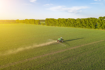 Aerial view of a farm tractor in a green field during spraying and irrigation with pesticides and...