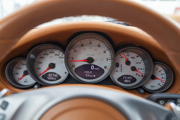 Dashboard is covered in beige genuine leather of a sports car with instruments speedometer and tachometer displays are highlighted on a black background with a red dial and and an arrow.