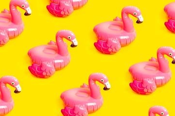 Creative summer beach concept. Pattern from Inflatable pink mini flamingo on yellow background, pool float party. Flat lay, copy space. Flamingo Trend Inflatable Toy. Summer background