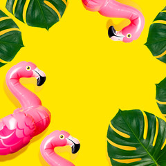 Creative summer beach concept. Inflatable pink mini flamingo and tropical leaf monstera on yellow background, pool float party. Flat lay copy space. Flamingo Trend Inflatable Toy. Summer background