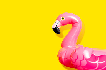 Creative summer beach concept. Inflatable pink mini flamingo on yellow background, pool float...