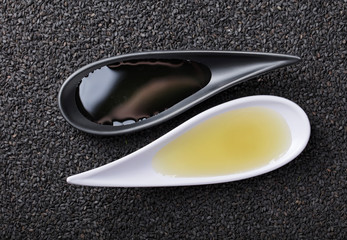 Sesame oil in small bowls on a background of black sesame.