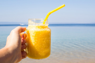 Fruit cocktail  in woman hand against tropical beach. Summer refreshment. Travel and vacation concept