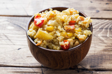 Pilaf with vegetables and chicken in wooden bowl on wooden background.