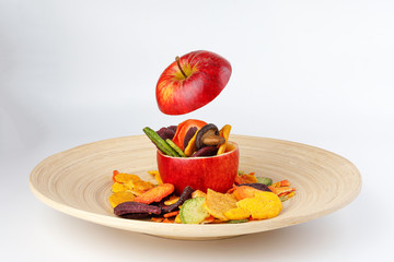 Healthy vegetable chips yellow sweet potato purple carrot green radish green beans and shiitake mushrooms in hollow red apple white background wooden plate