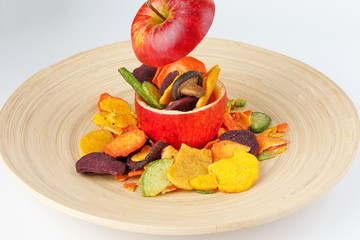 Healthy vegetable chips yellow sweet potato purple carrot green radish green beans and shiitake mushrooms in hollow red apple white background wooden plate