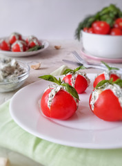 salad with cherry tomatoes and basil. Tomatoes stuffed with cheese and herbs, decorated with Basil on a round white plate on a light background.