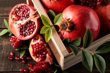 Ripe tasty red pomegranate fruit with leaves in a wooden box on a brown wooden table. top view - Powered by Adobe