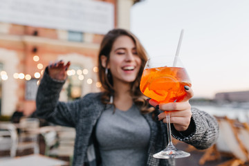 Beautiful brown-haired girl having fun in cafe and drinking fruit cocktails with pleasure. Outdoor...