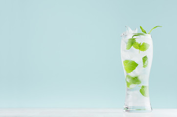 Fresh summer cold mint drink with green leaf, ice cubes, tonic in light soft pastel  blue color background on white wood board.