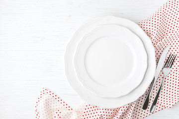 White empty plates and cutlery on polka dot napkin on white wooden table. Setting table top view.