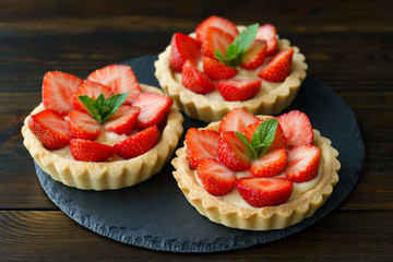 Tartlets with custard, strawberries and mint served on a slate plate
