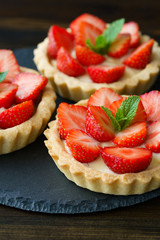 Tartlets with custard, strawberries and mint served on a slate plate