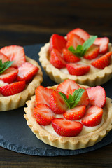 Tartlets with custard, strawberries and mint served on a slate plate