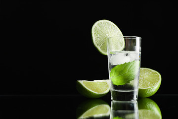 Tequila shot with lime, mint and ice against black background