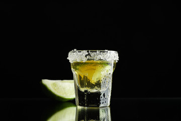 Tequila shot with lime and sea salt on black background