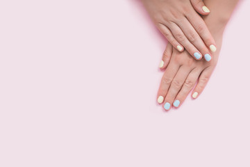 Fresh blue and yellow manicure on pink isolated background.
