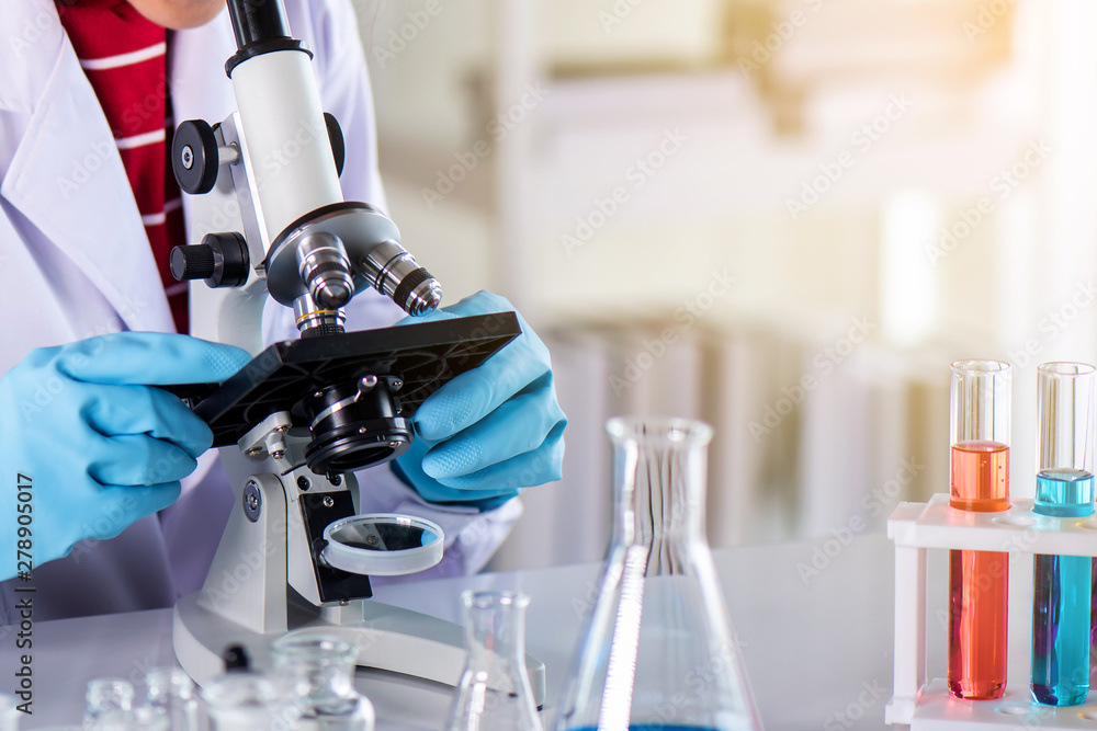 Wall mural scientist using microscope in laboratory with lab glassware containing chemical liquid, science or m
