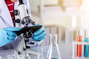 Scientist using microscope in laboratory with lab glassware containing chemical liquid, science or medical research and development concept 