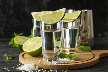 Tequila shots with lime slices, salt and mint on wooden background