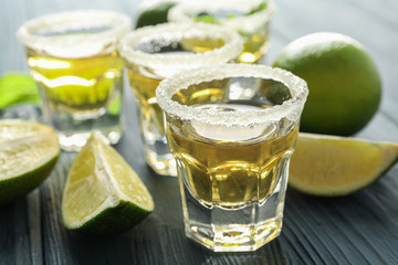 Tequila shots, salt, lime slices and mint on wood table, closeup