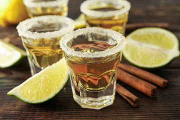 Tequila shots with salt, lime slices and cinnamon on wood table, closeup