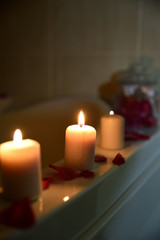 Obraz na płótnie Canvas Three candles in bathroom with rose petals, home spa scene