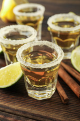 Tequila shots with salt, lime slices and cinnamon on wood table, closeup
