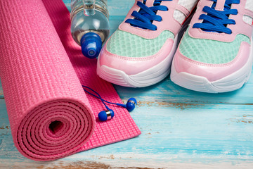 Fototapeta na wymiar Pink yoga mat, sport shoes, bottle of water and earphones on blue wooden background. Sport, healthy lifestyle, yoga concept. Trendy female sport equipment. Copy space