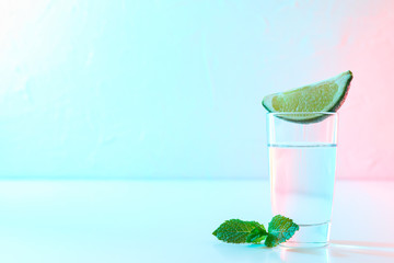 Tequila shot with lime slice and mint against white background with blue - pink light