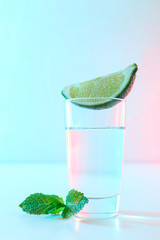 Tequila shot with lime slice and mint against white background with blue - pink light