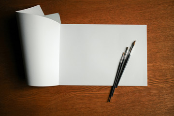 Paint brushes and album with blank paper for drawing on the wooden background